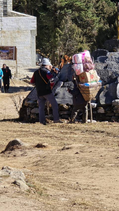       People with supplies and a yak in a mountainous village setting.
  