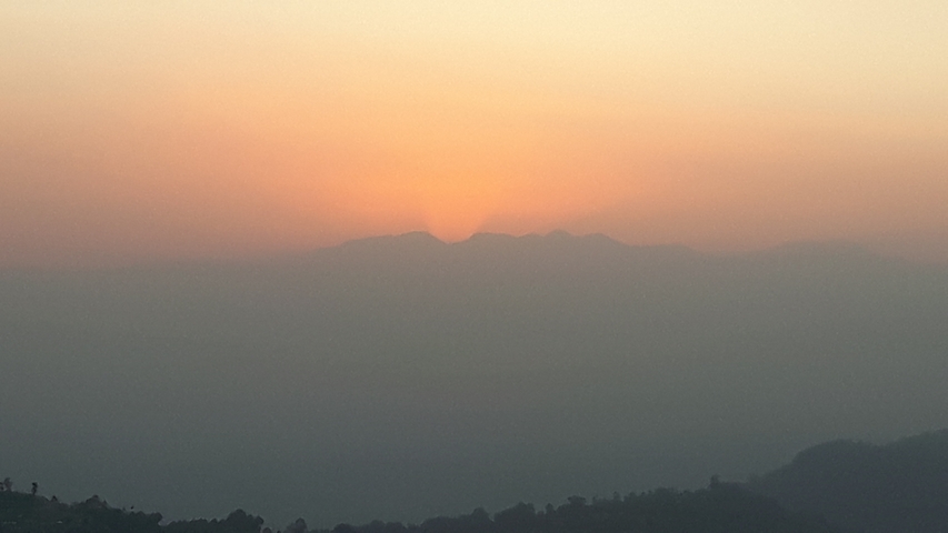       Sunset over a mountain range with a warm glow.
  