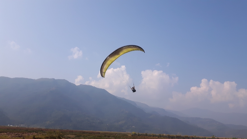       Paraglider soaring through mountains under a blue sky.
  