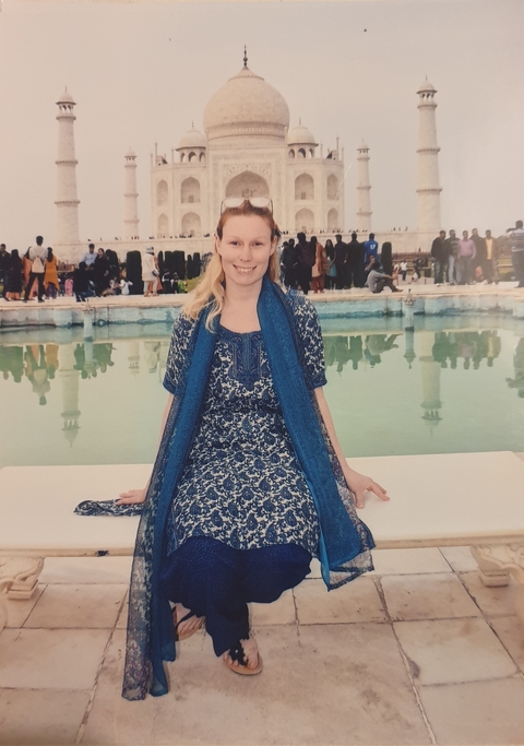 Woman posing in front of a reflective pool with people and minarets in the background.