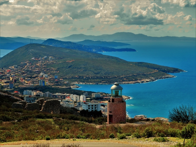       A coastal town with a lighthouse and sprawling mountain scenery.
  