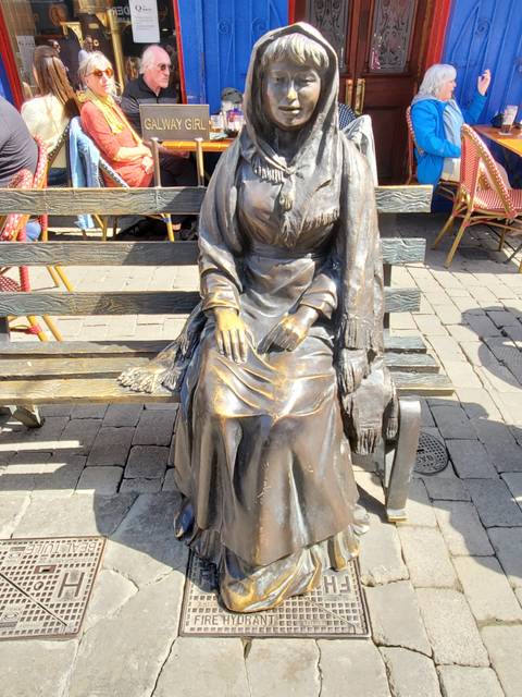       A bronze statue of a seated woman on a bench.
  