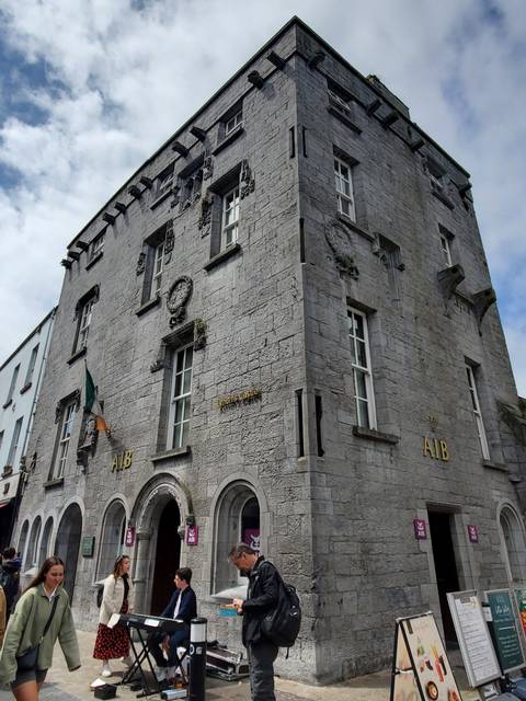 A street with an old building, people walking, and outdoor seating.
