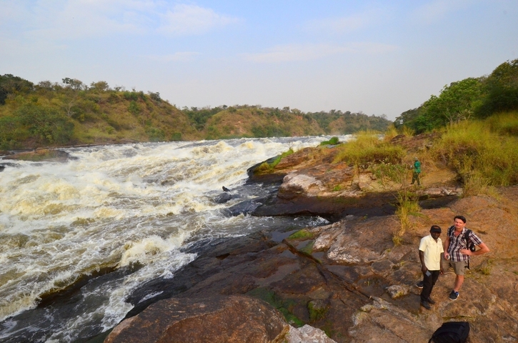 People walking along a riverbank with rapids.