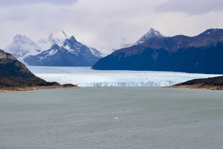 Snow-capped mountains and a glacier reaching a lake.