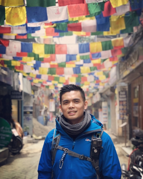 Man in a colorful street with prayer flags above.