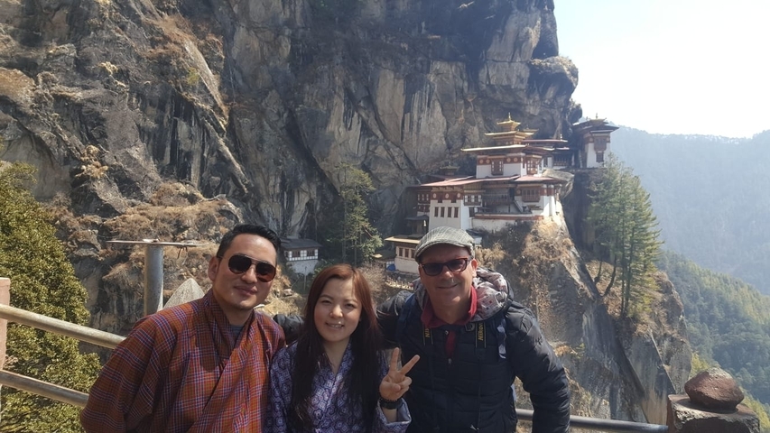 Three people posing in front of a cliff-side with a monastery.