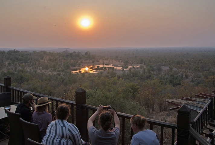       People observing a sunset over a waterhole in the savannah
  