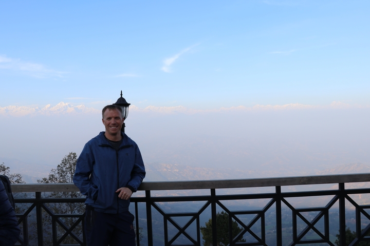       Man posing on a terrace overlooking misty mountains.
  