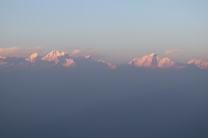      Close-up of sunlit snow-capped peaks against a pastel-colored sky.
  