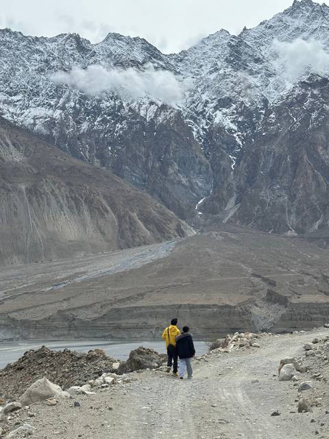       Two people walking on a rocky path with mountains in the distance.
  