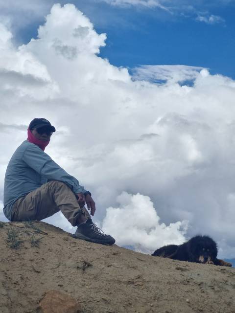       Person sitting on a slope with clouds in the background.
  