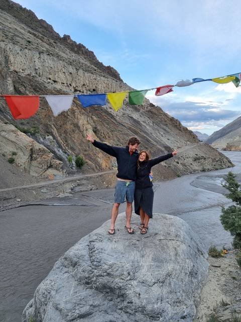 Two people standing on rocks near prayer flags.