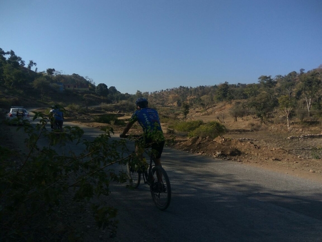       A person cycling on a road in a hilly landscape.
  
