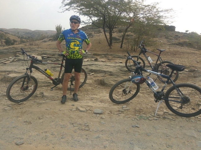       A person standing with bicycles in a rocky outdoor area.
  