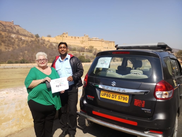 Two people posing with a car and a fort in the background.