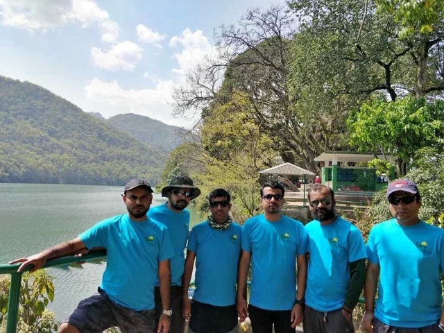       Group of six people in matching shirts posing by a lakeside.
  