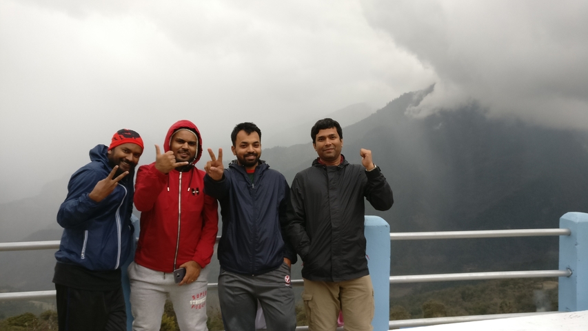       Four people in outdoor clothing posing with a cloudy mountain backdrop.
  