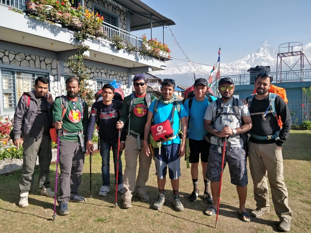 Group of hikers posing in front of a building with mountains.