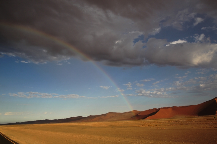 Rainbow across a desert landscape with dunes.