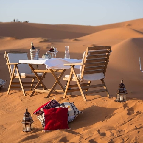 Elegant dining setup in the desert with dunes in the background.