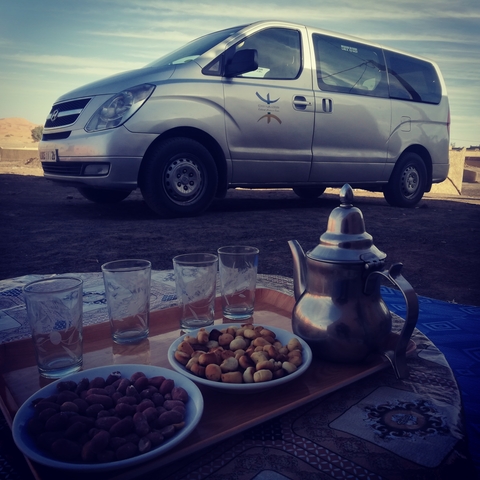 A tea set with glasses and snacks on a tray in front of a parked car.