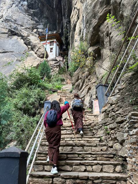 Two people hiking up stone steps toward a mountainside temple.