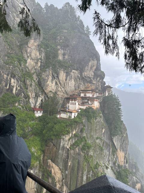Temple built into the side of a rocky cliff during rainfall.