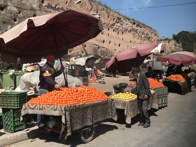       Fruit vendors selling oranges under umbrellas.
  