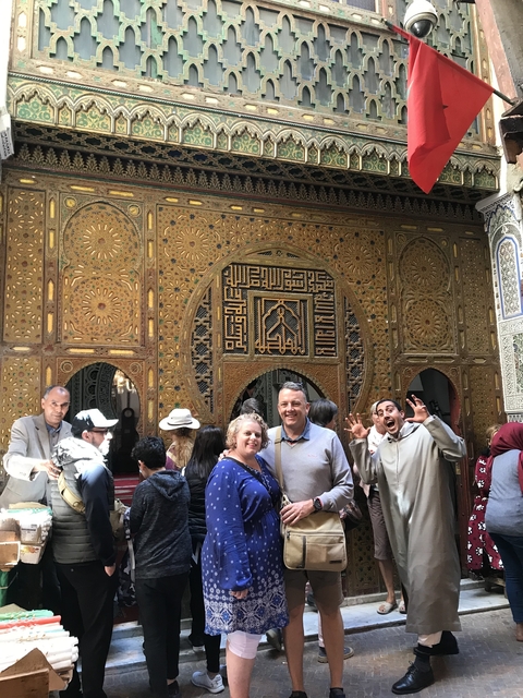 Group of people posing in front of a richly decorated door with Arabic inscriptions.