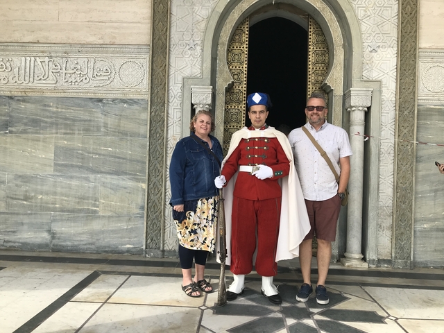       A couple posing with a guard in ceremonial uniform.
  