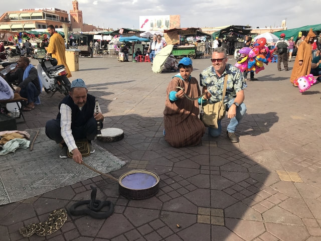       Snake charmer with cobras and a basket of performing snakes in a public plaza.
  