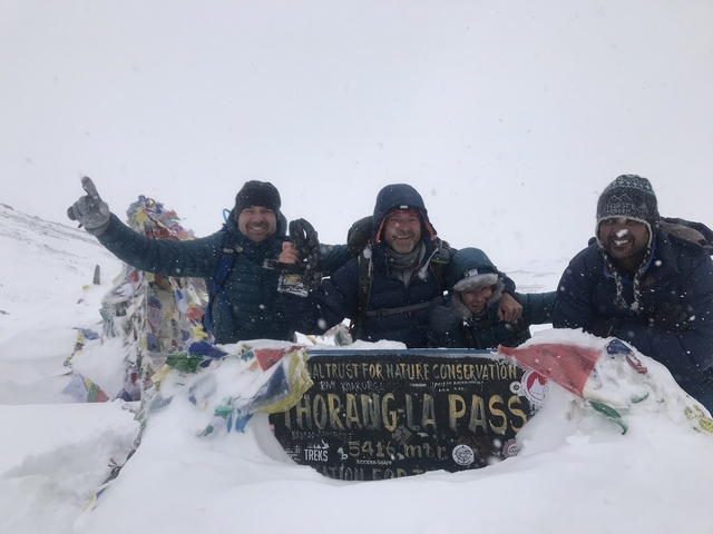 Group of people celebrating at Thorang La Pass covered in snow.