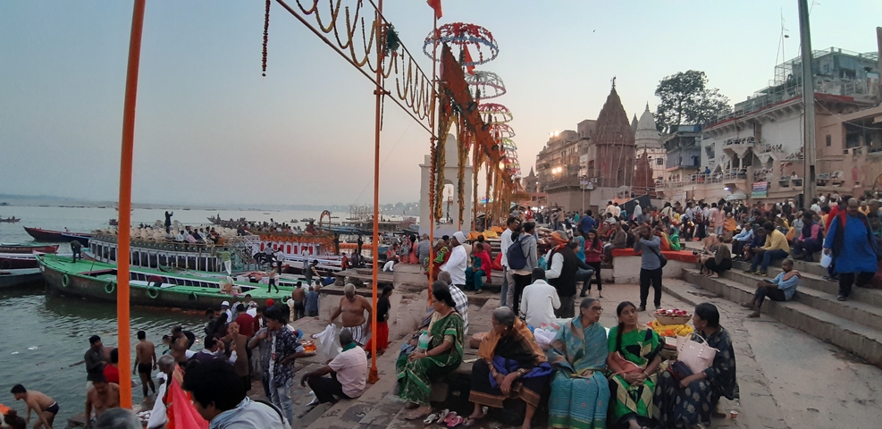 A busy riverbank scene with people and boats at a cultural event.