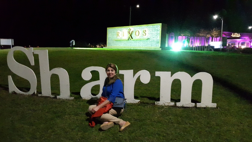       Person sitting in front of a decorative sign at night.
  
