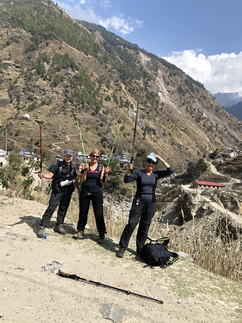 Three people with trekking poles in a mountainous area.