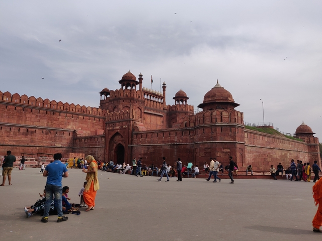 People walking near a large red sandstone fort complex.