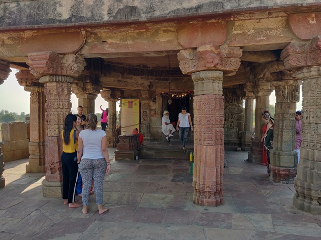       People visiting a temple with carved pillars.
  