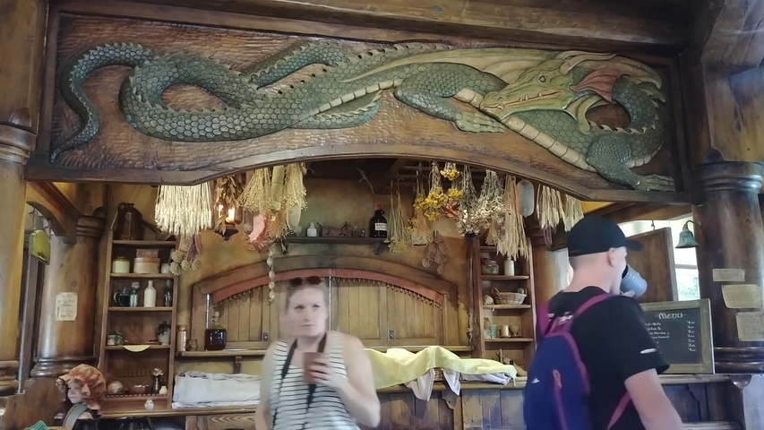 Inside a building with a wooden dragon carving and people walking.