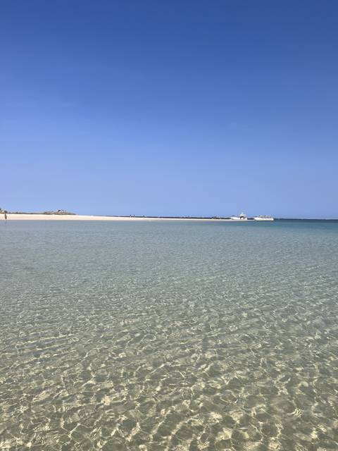 Shallow clear turquoise water with boats in the distance.