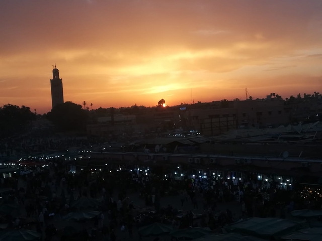 A busy square at sunset with a minaret in the background.