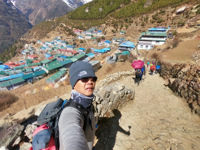       Person on a hiking trail overlooking a colorful mountainous village.
  