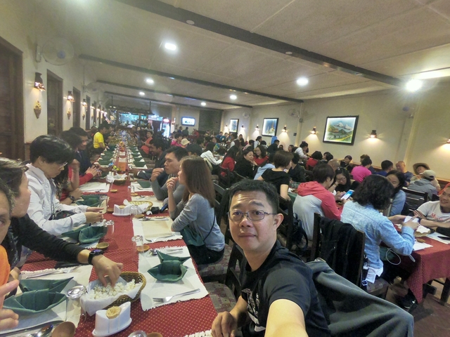       Dining hall with many people eating together at long tables.
  