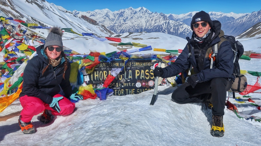       Two people at the Thorong La Pass with snow and prayer flags.
  