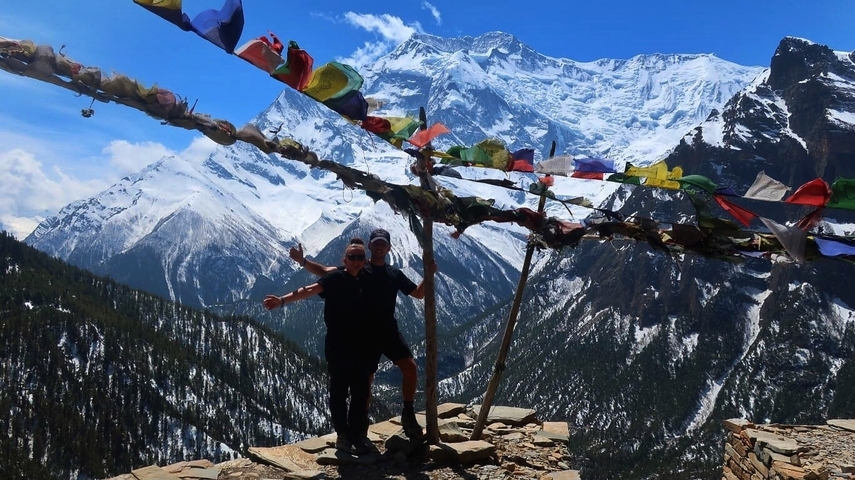       Two people standing on a viewpoint with mountains.
  