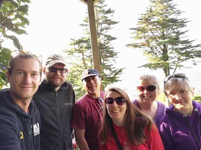       Group of friends posing at a lookout with trees behind.
  