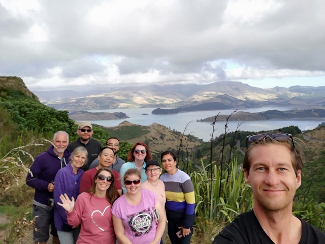       Group of people smiling with a scenic backdrop of hills and a bay.
  