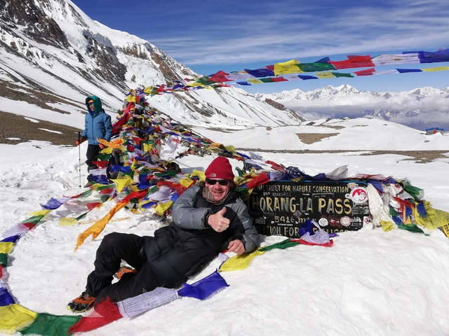       Hiker posing with prayer flags and a sign
  