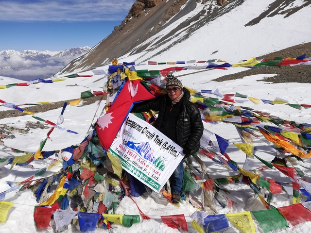       Person posing with a flag and prayer flags in a snowy area
  