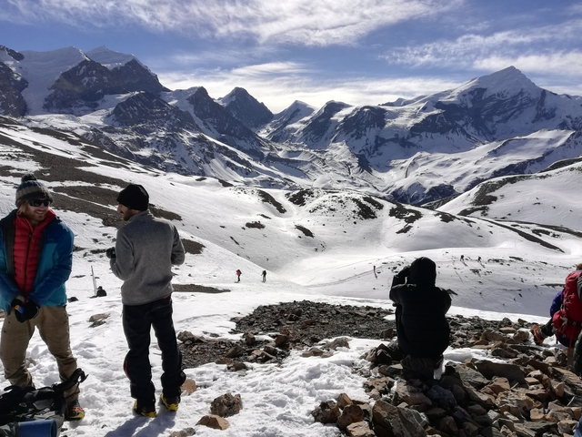       Group of people on a snowy mountain with peaks in the background
  